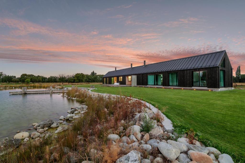 a house with a black roof next to a pond at Lyford Luxury Lodge, Twizel in Twizel