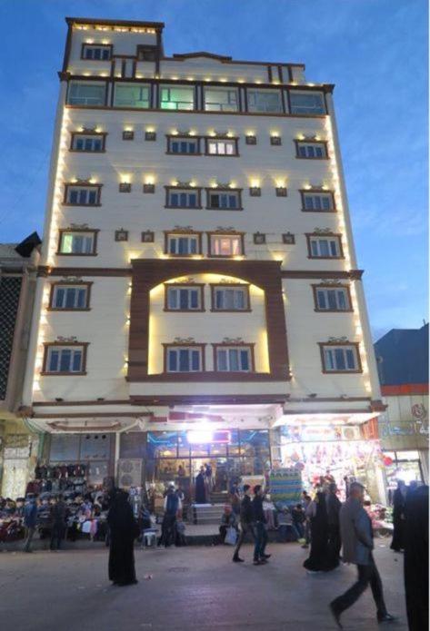 a tall building with people walking in front of it at Hotel Janat Al Naim in Karbala