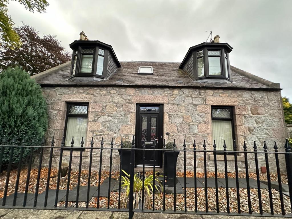 una vecchia casa in pietra con due finestre e una recinzione di Ann Cottage Retreat in Aberdeen ad Aberdeen