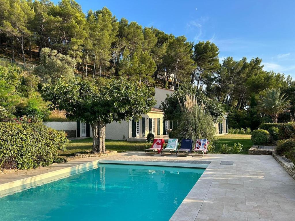 une piscine avec deux chaises et une maison dans l'établissement Villa La Ventilière pour 12 Personnes avec Piscine Chauffée, Terrain de Tennis, de Pétanque et Vue Mer, au Beausset
