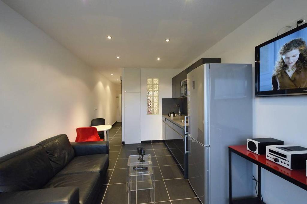 Il comprend un salon avec un canapé en cuir noir et une cuisine. dans l'établissement Studio ELLE et LUI Port Nature PN830 - Luxe - 2 personnes, au Cap d'Agde