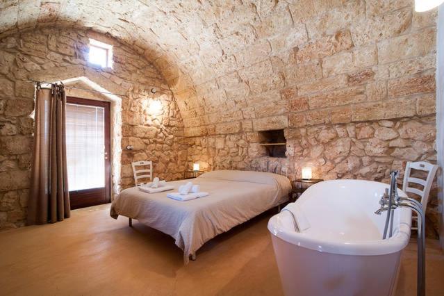 a bedroom with a bed and a bath tub in a stone wall at Agriturismo Le Fornelle in Tricase