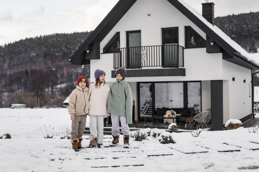three children standing in the snow in front of a house at Bieszczadzka Wataha in Paszowa