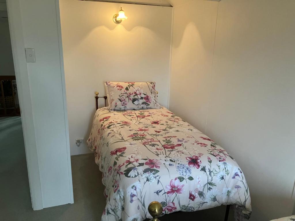 a small bedroom with a bed with a floral comforter at Rose Cottage in Hamilton
