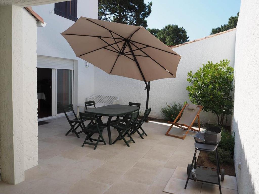 un patio avec une table, des chaises et un parasol dans l'établissement Villa 4 chambres près de la plage avec parking à La Palmyre - FR-1-705-95, aux Mathes
