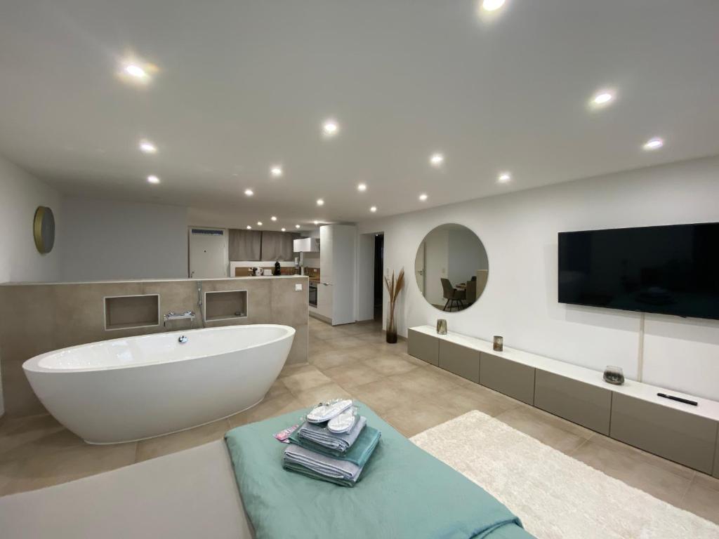 une salle de bain avec une grande baignoire blanche et une télévision dans l'établissement Terrassenpark Apartments (Premium Rooms), à Sasbachwalden