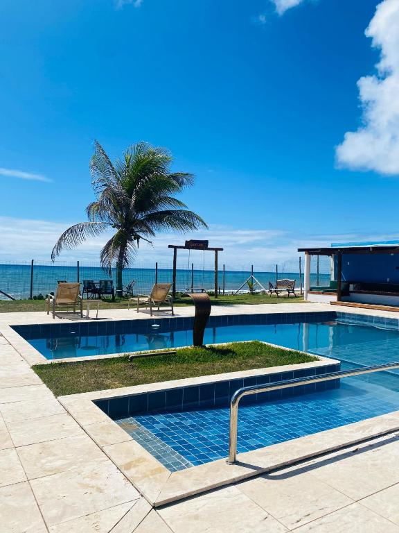 a swimming pool with a palm tree and the ocean at Pousada Destino in Porto de Sauipe