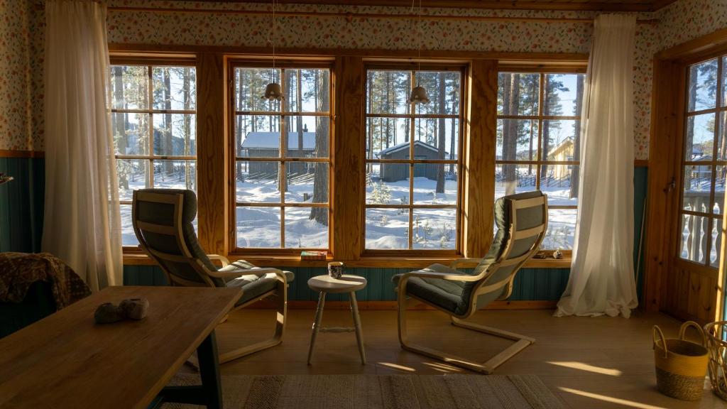 een kamer met een tafel, stoelen en ramen bij Sunshine Stuga Mörtsjön in Stugun