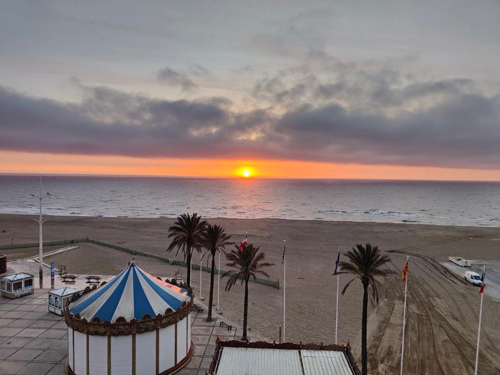 - un coucher de soleil sur une plage avec une tente et des palmiers dans l'établissement Front de Mer idéal classé 3 étoiles, à Canet