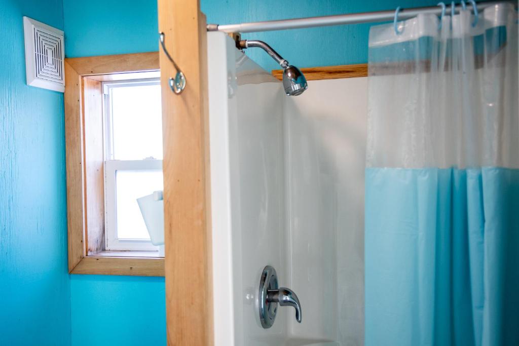 a bathroom with a shower with a mirror and a window at The Zzzz Moose Camping Cabins in Birch Plain