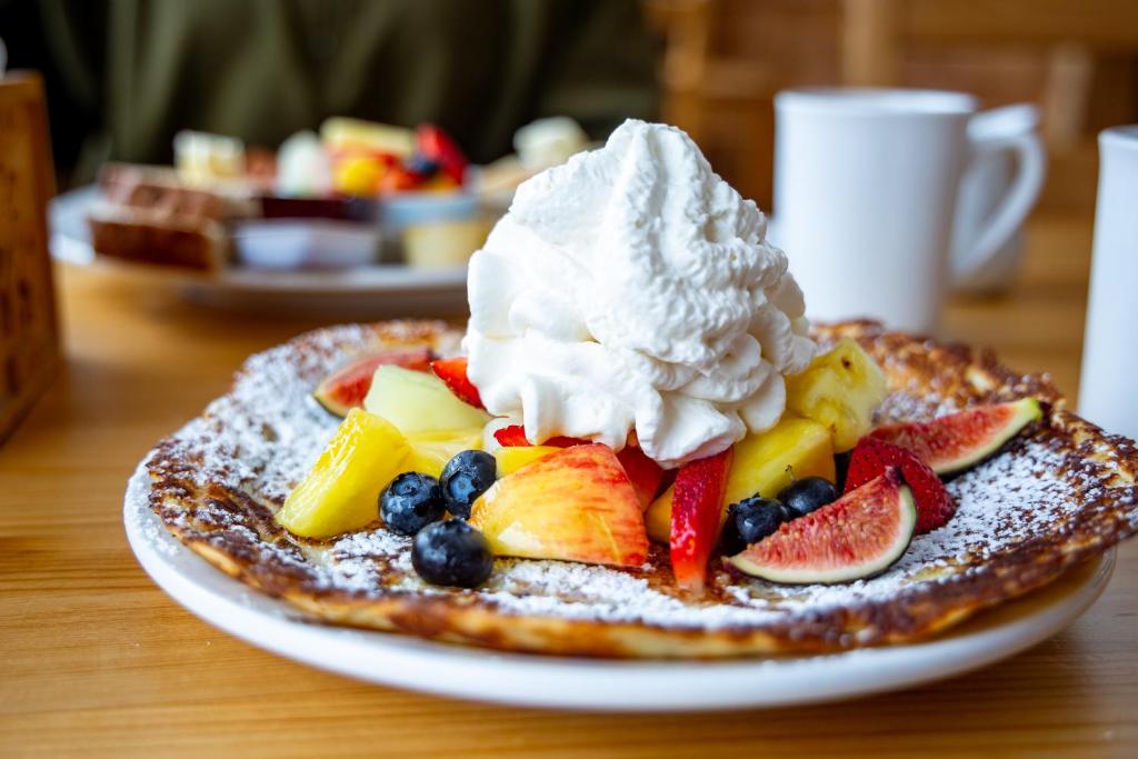 a plate of pancakes with fruit and whipped cream at The Zzzz Moose Camping Cabins in Birch Plain
