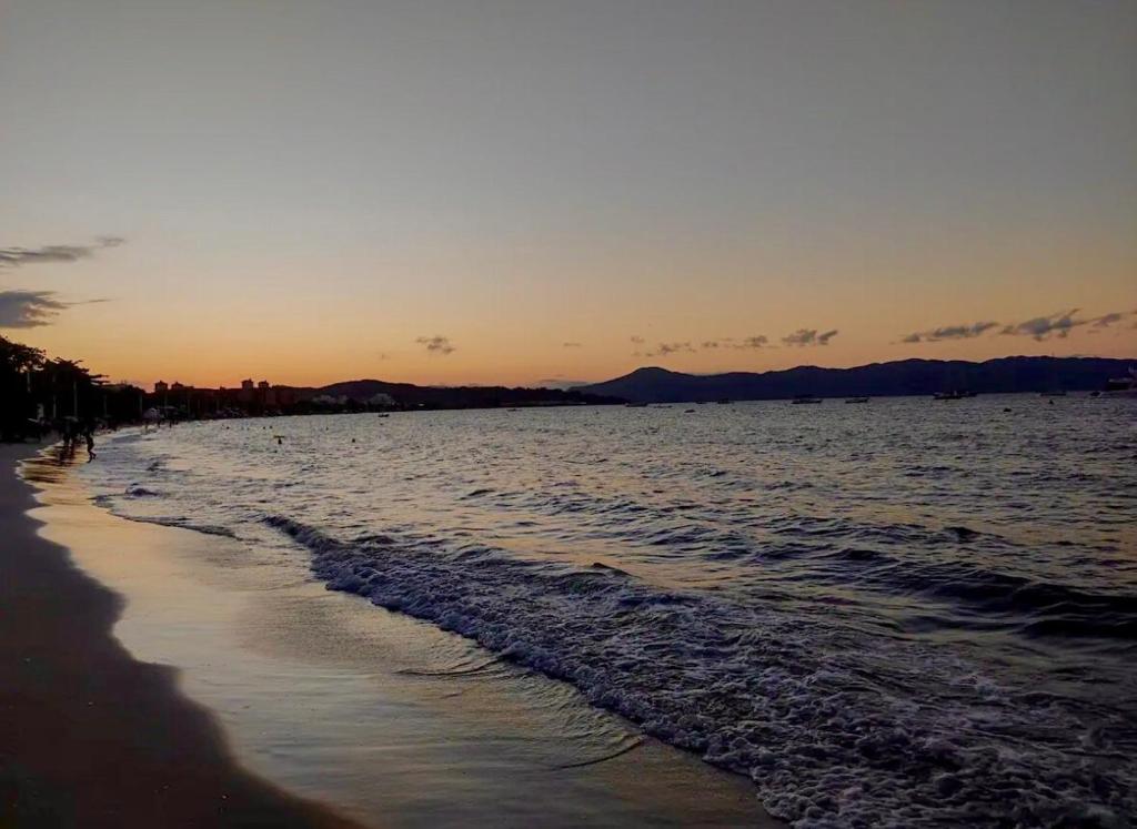 a beach with the sun setting on the water at Ap 50m do Mar, no Coração da Praia de Fora in Palhoça