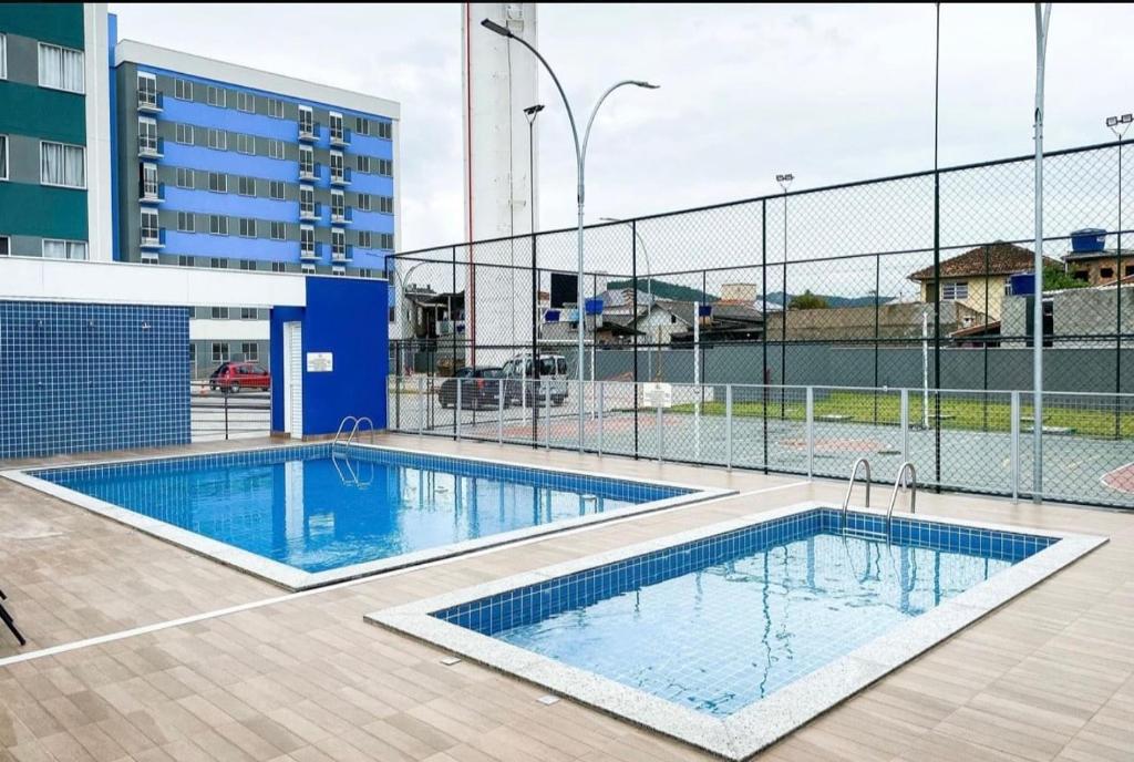 a swimming pool in front of a building with a fence at Ap 6 minutos da Praia de São Miguel, Em Biguaçu in Biguaçu