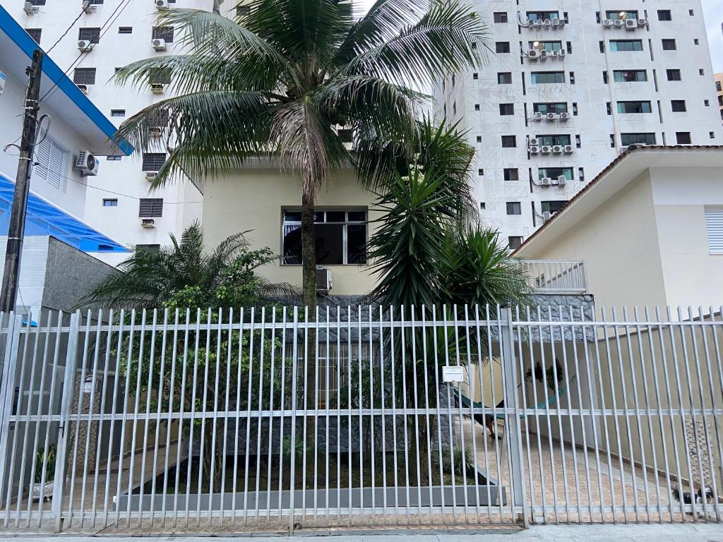 a white fence with a palm tree in front of a building at Confortável Casa em Pitangueiras no Guarujá in Guarujá