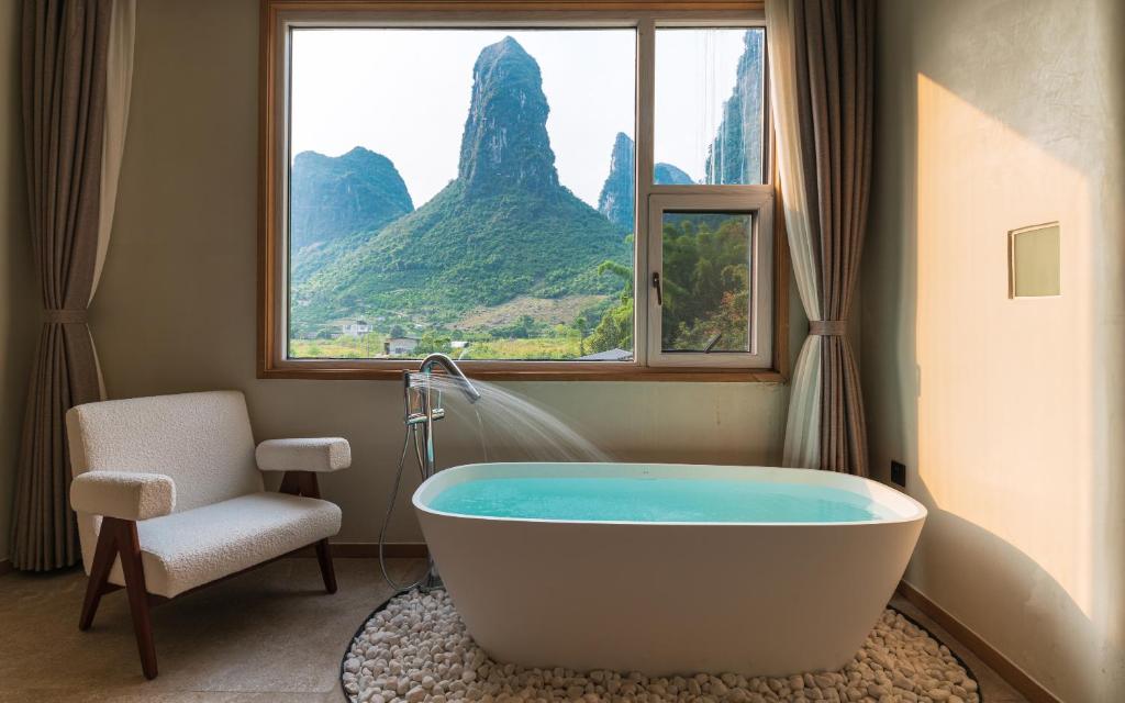 a bathroom with a tub and a chair and a window at Yangshuo One Thousand and One Courtyard Views B&B in Yangshuo
