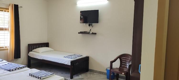 a room with two beds and a tv on the wall at Shri Ganesh Residency And Restaurant in Dharmastala