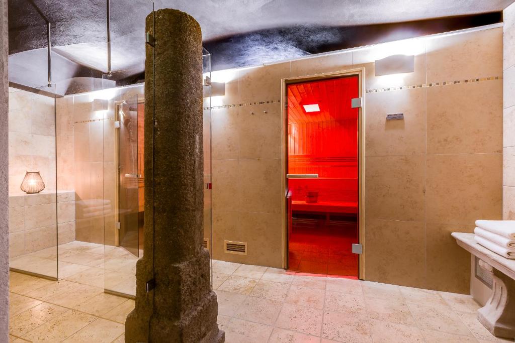 Tiled spa room with central stone pillar, glass shower panels and red-lit sauna doorway.