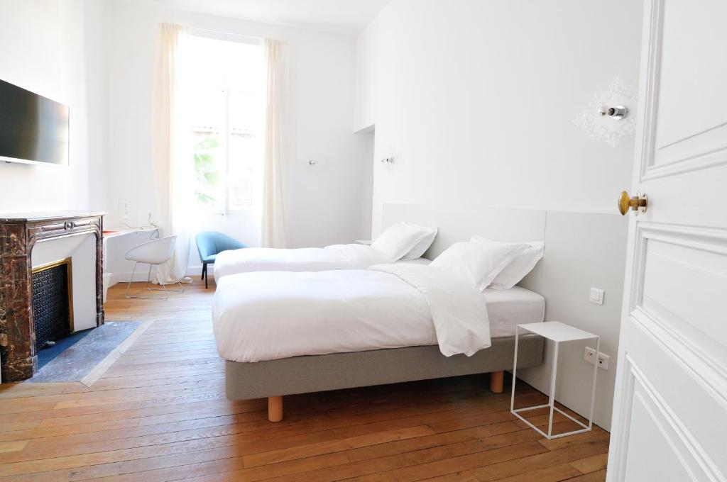 a white bedroom with two beds and a fireplace at L'Hôtel Particulier Beziers in Béziers