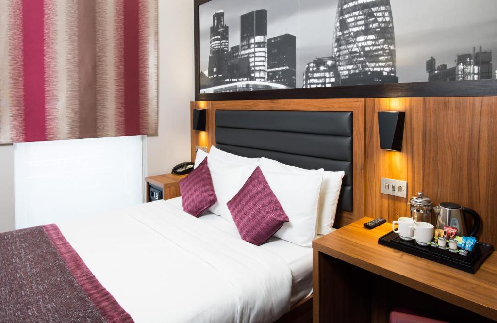Habitación de hotel con cama con sábanas blancas y almohadas moradas. en London Court Hotel en Londres