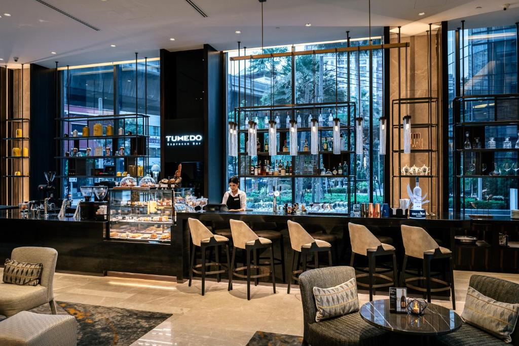 A polished hotel bar with counter seating, lounge chairs and tall windows.