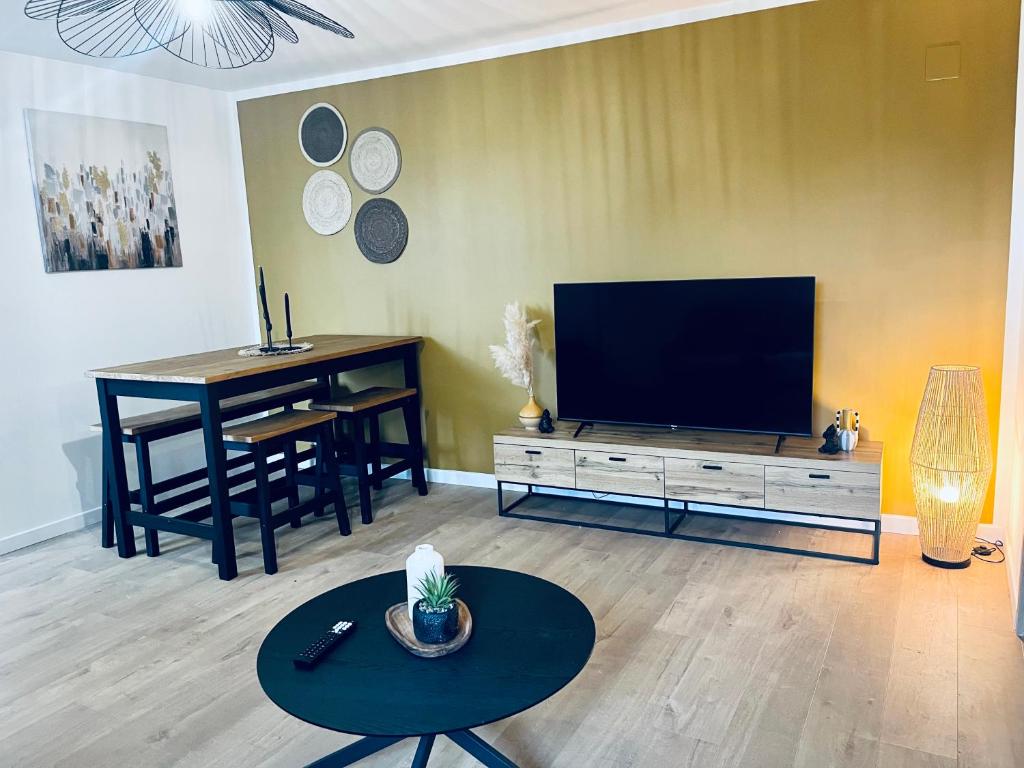 un salon avec une télévision à écran plat et une table dans l'établissement Le Pattulacci, à Rocroi