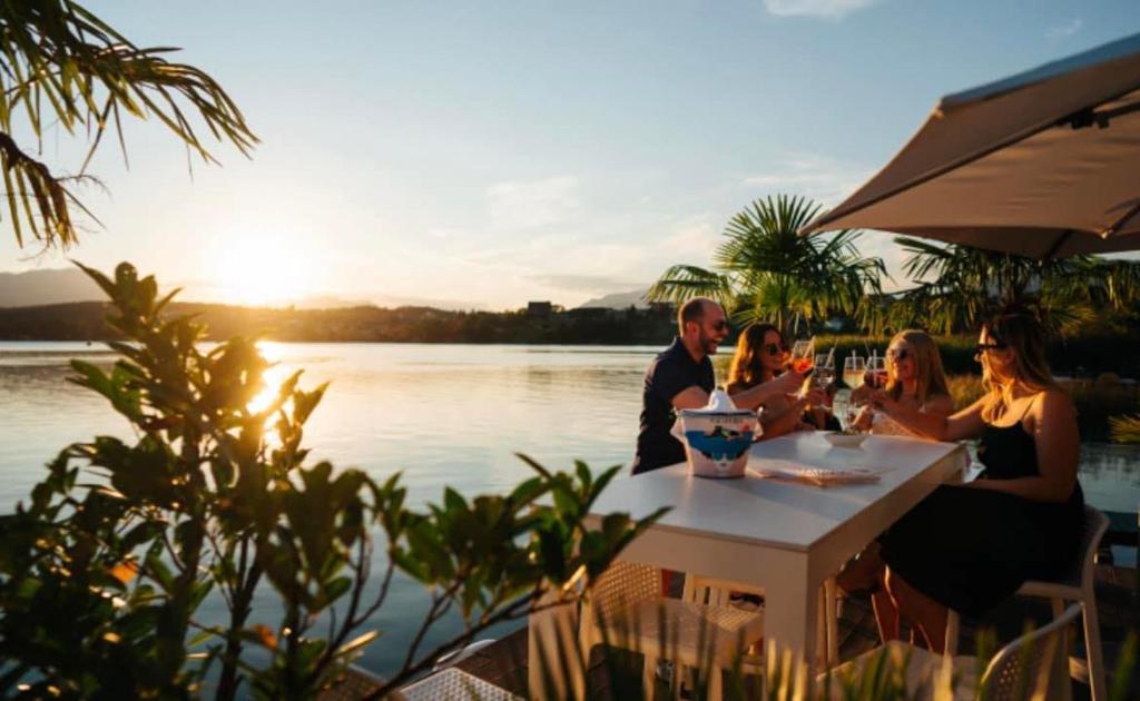a group of people sitting at a table by the water at Ville Bianche in Drobollach am Faakersee