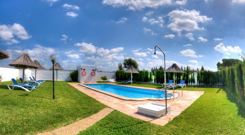 einen Pool im Garten mit Stühlen und Sonnenschirmen in der Unterkunft Hacienda los Majadales in Conil de la Frontera