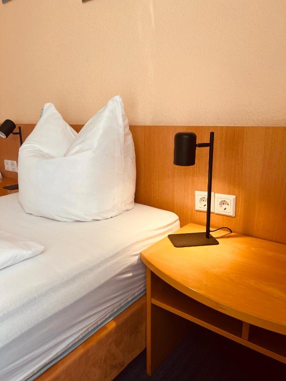 Una cama con una almohada blanca y una lámpara sobre una mesa. en TM Apart Hotel Essen, en Essen