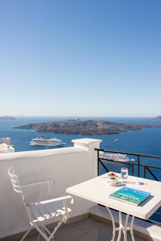 a white table and chairs on a balcony with the ocean at Villa Renos Hotel in Fira