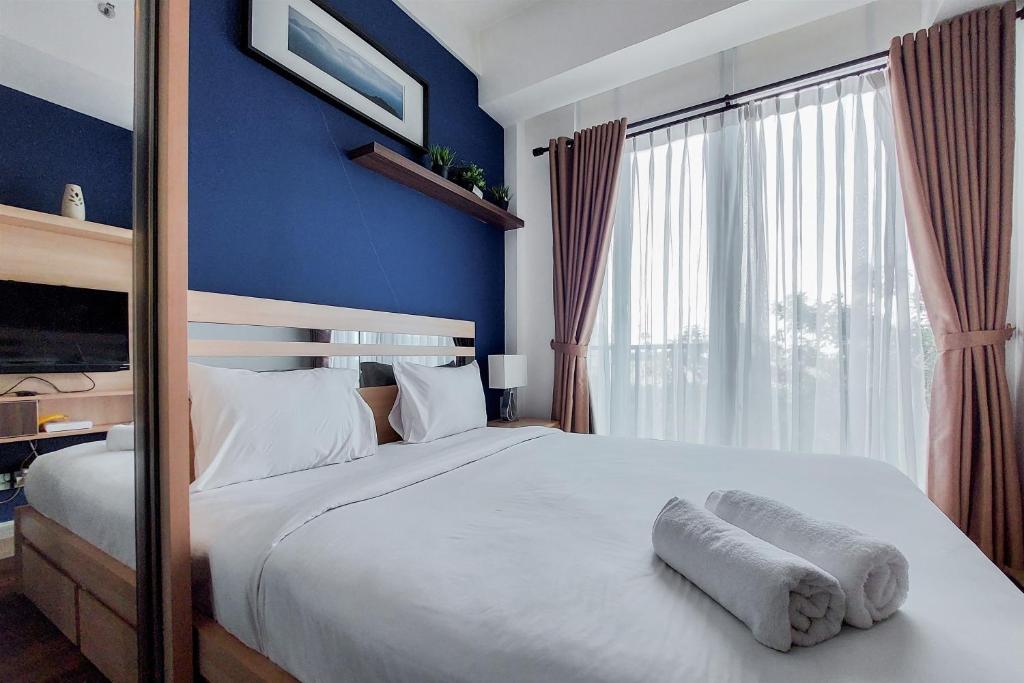 a bedroom with a large white bed with a blue wall at Nice and Elegant Studio at Tree Park City BSD Apartment By Travelio in Tangerang