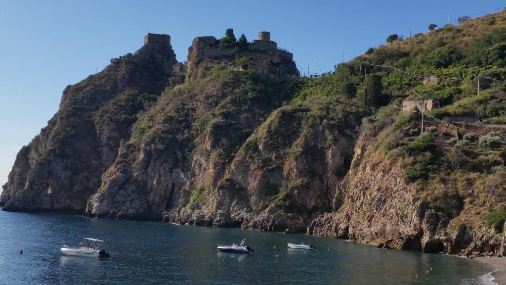 drie boten in het water naast een berg bij Caccia Apartment in Santa Teresa di Riva