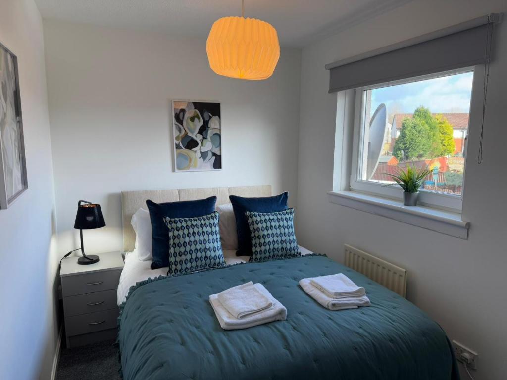 a bedroom with a bed with blue pillows and a window at Signature - Thorn House in Coatbridge