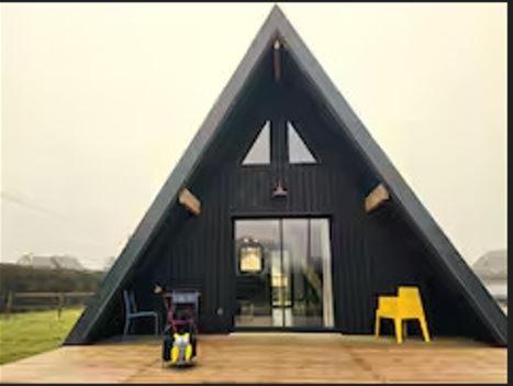 une maison noire avec un toit triangulaire et des chaises jaunes dans l'établissement le chalet d'hibs, à Montreuil-le-Chétif