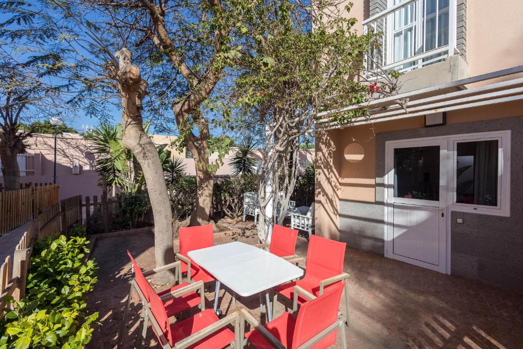 a table and red chairs on a patio at Bungalow Chill Terrace in Maspalomas & Pool in San Bartolomé de Tirajana
