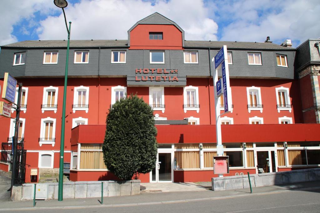 a red hotel with a tree in front of it at Hôtel Lutetia in Lourdes