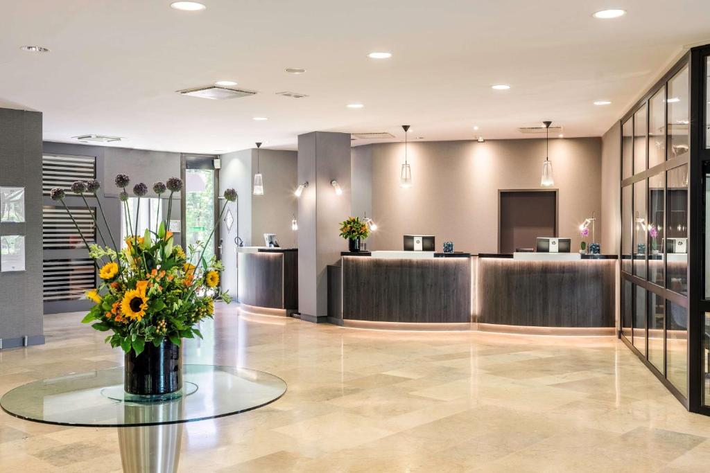 a lobby with a waiting area with a vase of flowers at NH Luxembourg Airport in Luxembourg