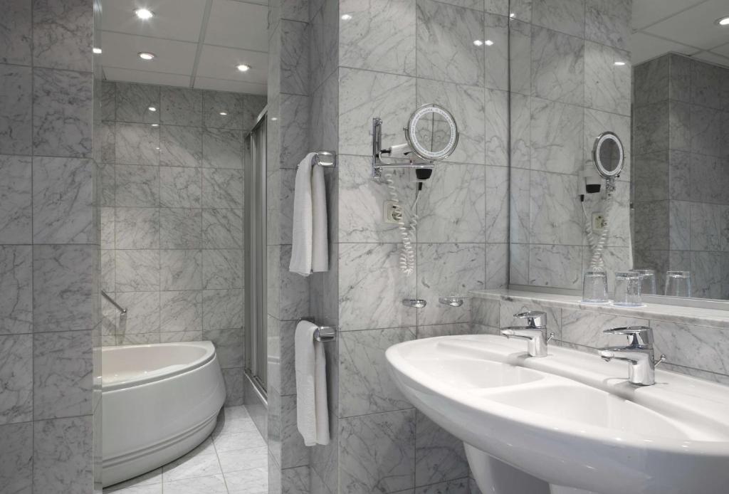a bathroom with two sinks and a toilet and a mirror at NH Luxembourg Airport in Luxembourg