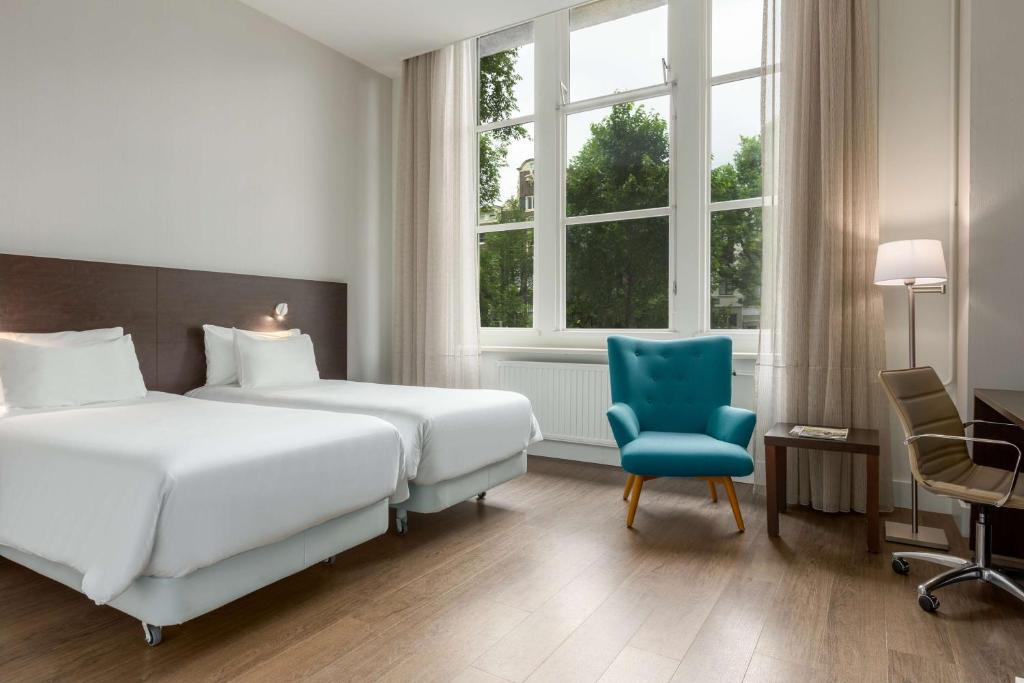 a hotel room with two beds and a blue chair at NH City Centre Amsterdam in Amsterdam