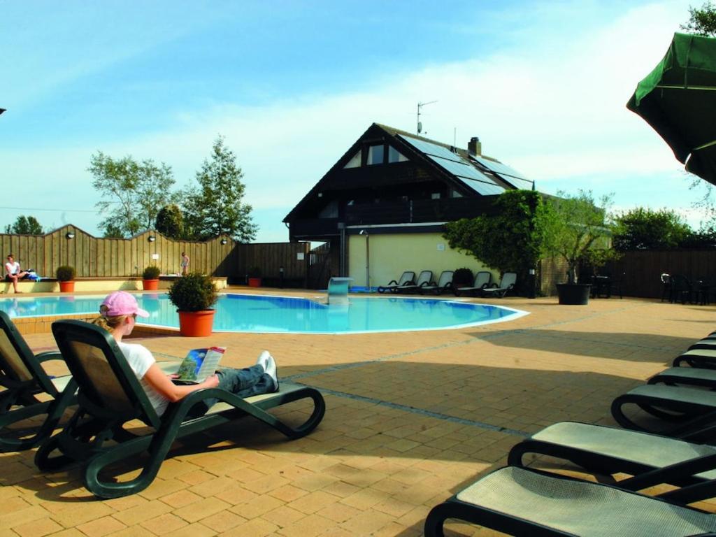 a man sitting in a chair reading a book near a pool at Holiday apartment F995 at Wulfener Hals, Fehmarn in Wulfen auf Fehmarn
