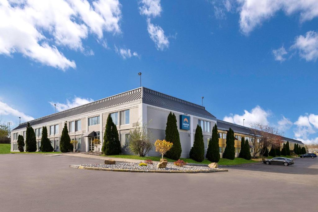 ein großes weißes Gebäude mit Bäumen auf einem Parkplatz in der Unterkunft Suburban Studios Syracuse Fairgrounds in Syracuse