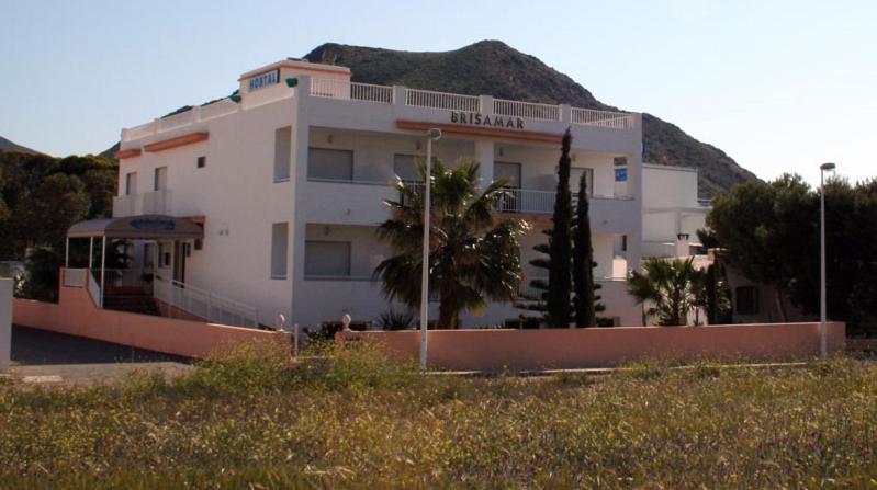 a large white building with a hill in the background at Hostal Brisamar in San José