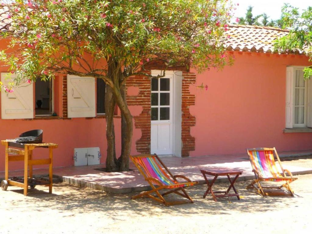 2 chaises, une table et un arbre en face d'une maison dans l'établissement Les pins, à Villeneuve-de-la-Raho