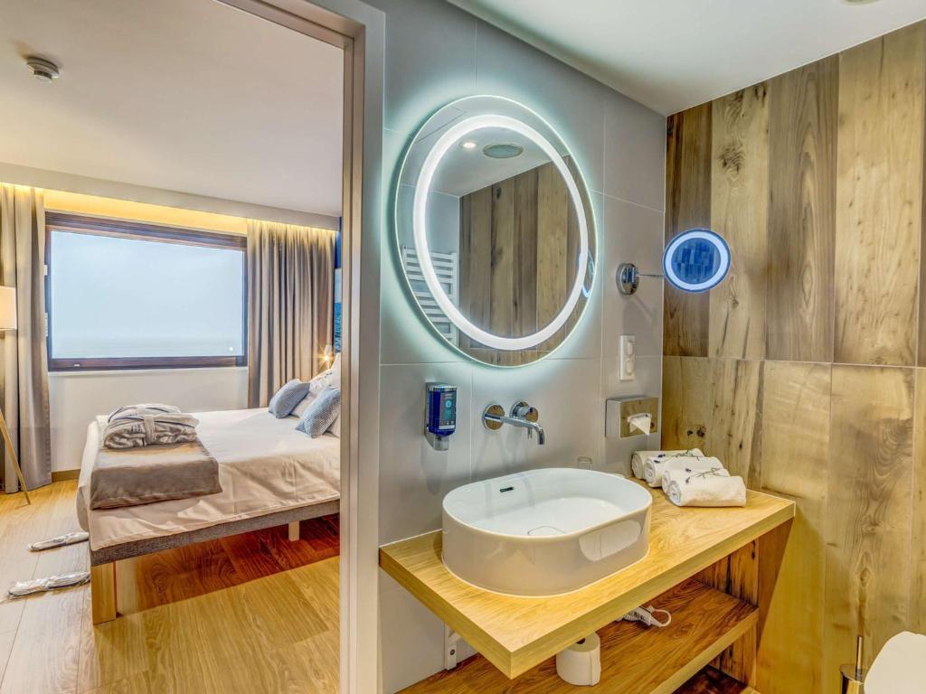 a bathroom with a sink and a mirror and a bed at Novotel Gdańsk Marina in Gdańsk
