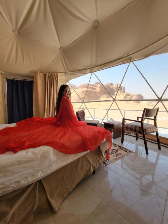 een vrouw in een rode jurk zittend op een bed bij MAXIMAS lUXURY WADI RUM in Wadi Rum