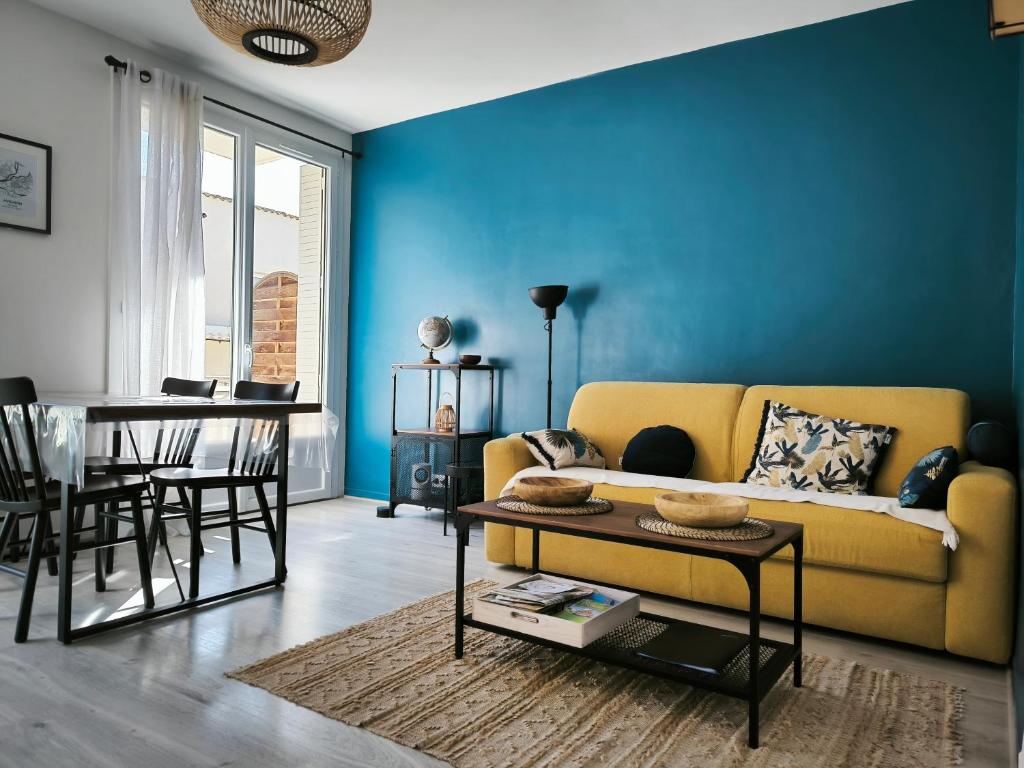 un salon avec un canapé jaune et un mur bleu dans l'établissement L'échappée belle, parking, climatisation, 5min à pied du centre historique, à Avignon