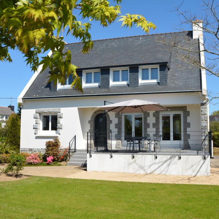 Cette maison blanche dispose d'une terrasse couverte avec un parasol. dans l'établissement La Villa Mana, à La Forêt-Fouesnant