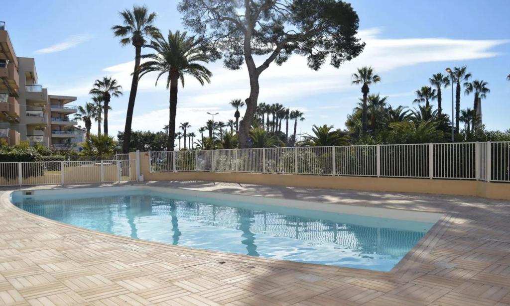 a swimming pool with a fence and palm trees at Charmant studio avec terrasse, front de mer et proche du centre in Saint-Raphaël