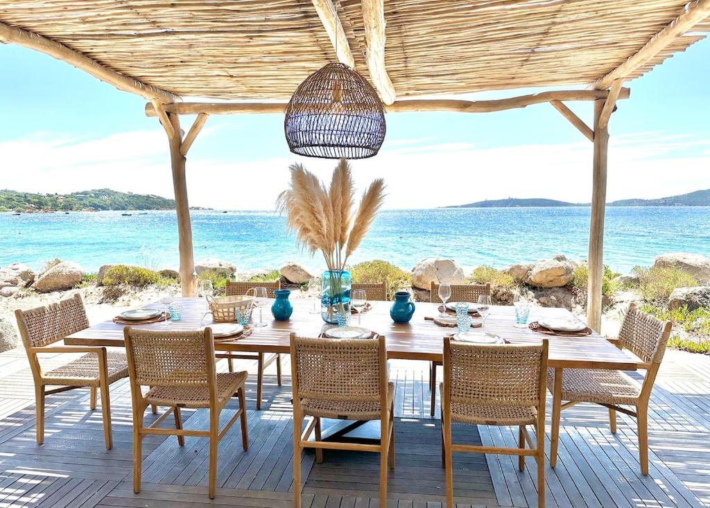- une table à manger et des chaises sur une terrasse donnant sur l'océan dans l'établissement Villa Cala Rossa pieds dans l'eau Porto-Vecchio, à Lecci