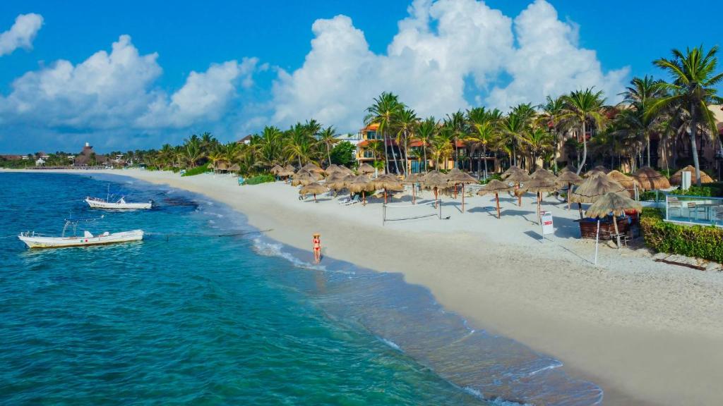 a beach with umbrellas and a boat in the water at Grand Oasis Tulum Riviera - All Inclusive in Akumal