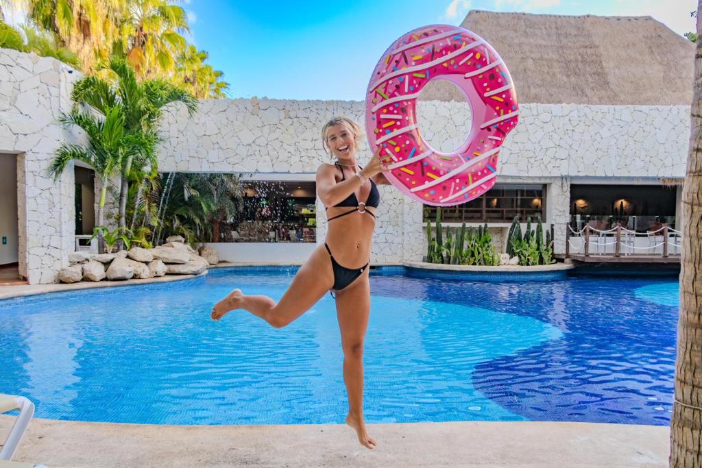a woman in a bikini jumping in a pool with a donut at Grand Oasis Tulum Riviera - All Inclusive in Akumal